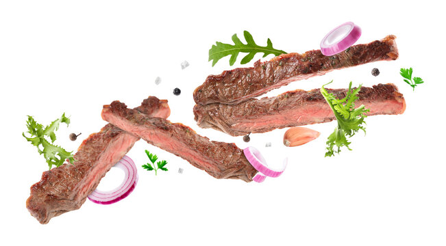 Roasted beef pieces, herbs, onion and garlic flying in air on white background