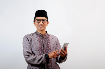 An Asian Muslim man smiles happily while sending a message using his mobile phone, isolated on white background