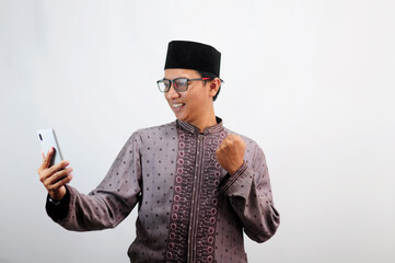 An Asian Muslim man smiles happily while sending a message using his mobile phone, isolated on white background