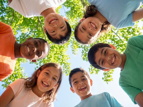 Low angle view of diverse happy children standing in a circle smiling down at the camera outdoors