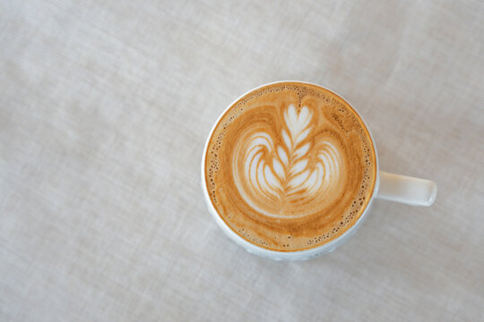 Top view hot coffee latte art flower shape in ceramic cup on cream colored fabric background. Copy space.