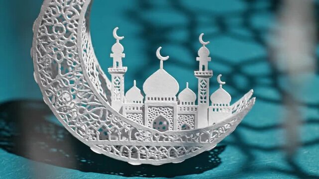 Intricate white paper cutout of mosque silhouette resting inside crescent moon on bright background