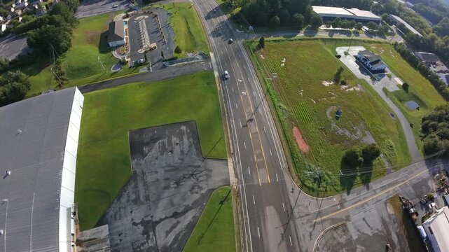Johnson City, USA Overhead Johnson City Suburban Corridor Intersection, Early Morning Traffic Along Four Lane Road, Warehouse Roof And Paved Lots, Green Median And Circular Planting Bed,