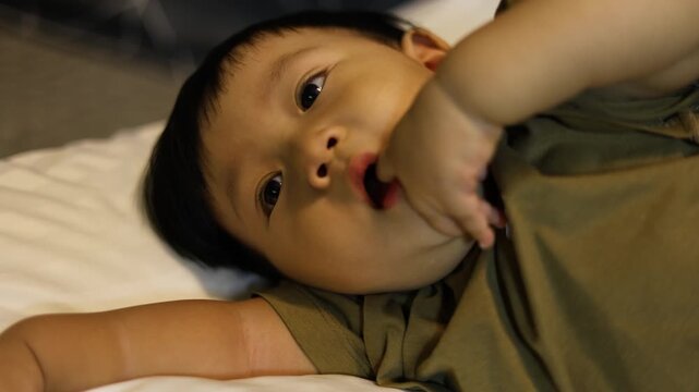 Toddler Putting Finger in Mouth. A curious toddler lies down, fingers probing new teeth with a gleeful, bathed in soft nursery, perfect for a cozy home video or a parenting joy showcase.