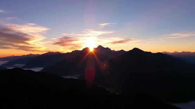 Sunrise over silhouetted mountains light beams radiating from behind the peaks clouds tinged with orange