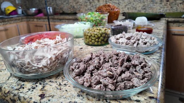 tracking out movement revealing an organized mise en place of beef, chicken, olives, and fresh vegetables for the traditional preparation of Christmas hallacas.