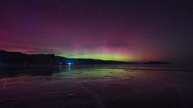 Red-green aurora borealis in the starry sky, reflected on the ice of the lake