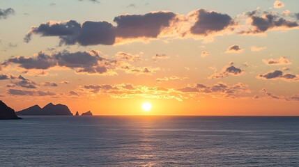 Sun setting over ocean horizon with distant islands and clouds