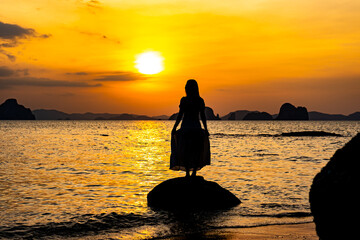 Beautiful young woman silhouette standing on stone at sunset or sunrise sky over sea