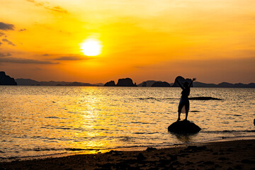 Beautiful young woman silhouette standing on stone at sunset or sunrise sky over sea
