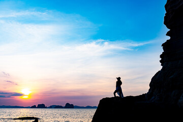 Beautiful young woman silhouette standing on stone at sunset or sunrise sky over sea