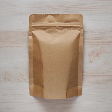 Isolated Kraft Paper Pouch Mockup on Light Wood. Sustainable Packaging & Eco-Friendly Product Shoots. Biodegradable zipper pouch made of natural kraft paper on a unfinished light oak wood surface.
