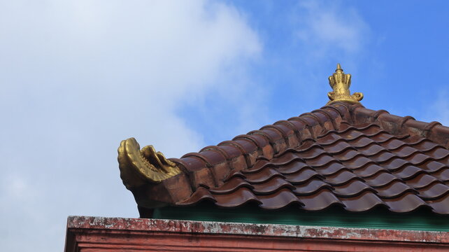 Decorations made of baked clay and golden yellow are attached to the roof of a traditional Javanese house.