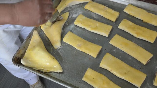 BRUSHING THE CREAM-FILLED EMPANADAS WITH EGG