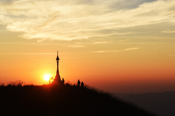 Silhouette of a Buddhist pagoda and people on a mountain peak at sunset with a beautiful golden sky.