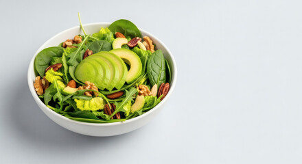 Green salad bowl with avocado and nuts, minimal background, copy space