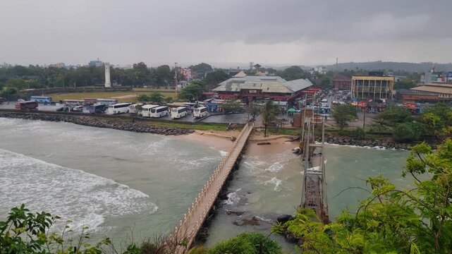View of Matara&rsquo;s old and new Paravi Duwa Bridges on a rainy monsoon day, with Indian Ocean waves hitting the shore and the bus station visible across, filmed from the temple