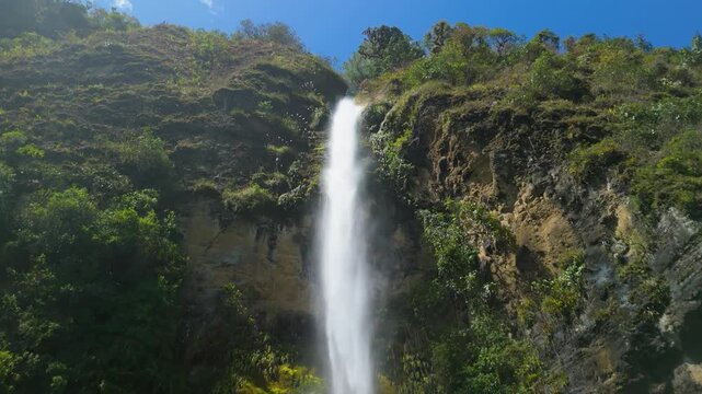 Flying close to edge of high rocky cliff as water plunges down Chorro del Giron waterfall surrounded by lush tropical forest in Azuay