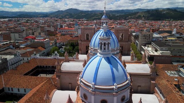 Cinematic drone shot circles famous patterned ceramic domes and brick architecture of Cathedral of the Immaculate Conception under blue sky in historic city center of Cuenca