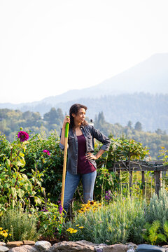 Young woman of color leaning on shovel in her beautiful garden