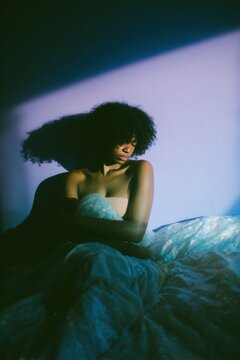 Young Black Woman in Bed Looking Down with Stomach Pain for Endometriosis Awareness and Womens Healthcare Concepts in a Moody Purple Bedroom Seeting