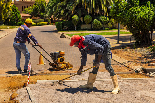 Two african american construction workers leveling gravel during road paving, vibratory plate compactor