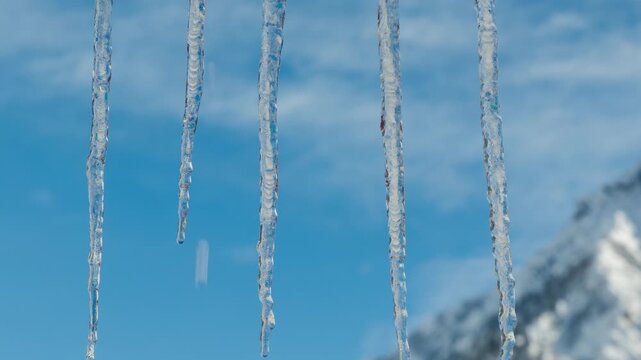 Motion controlled Time Lapse reveal of melting icicles hanging from roof with Snowy Mountain Peak and Moving Clouds in the background. 