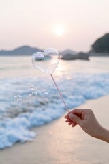 Hand holding heart shaped bubble wand at beach sunset
