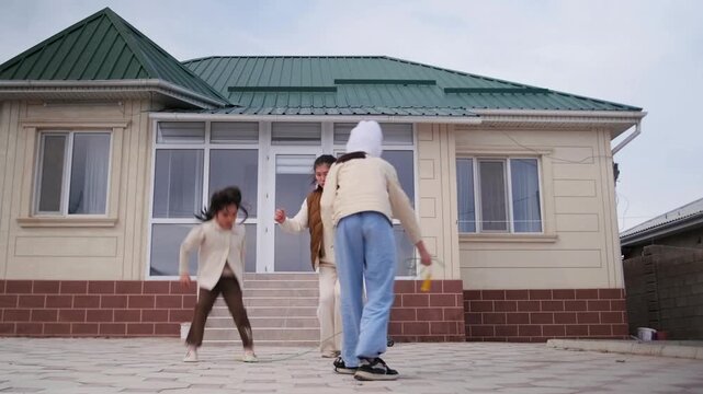 Two kids play with skipping rope in front of modern house. Active childhood, outdoor fun, and sibling activity on bright day. Family lifestyle and happy childhood moments.. Authentic everyday lifest