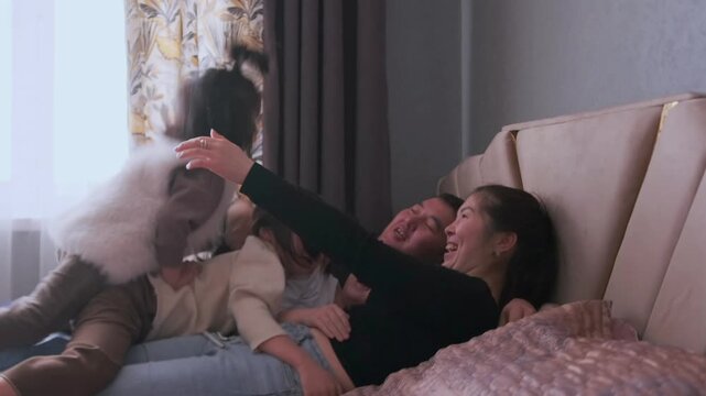 Asian parents and children laughing and playing on bed in morning. Authentic everyday lifestyle moment, natural behavior captured indoors, cinematic shot emphasizing real life emotions and daily rou