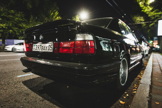 Back view showing the iconic taillights and spoiler of a black BMW E34 on an urban street. Almaty, Kazakhstan - October 04, 2024