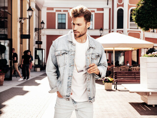 Fototapeta premium Portrait of handsome confident stylish hipster lambersexual model. Sexy man dressed in jeans jacket. Fashion male posing in the street in sunglasses in Europe city. Outdoors at sunset
