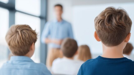 Fototapeta premium In a lively classroom setting, several faceless elementary students sit at their desks, attentively focusing on their teacher as he shares knowledge. Sunlight streams through the windows