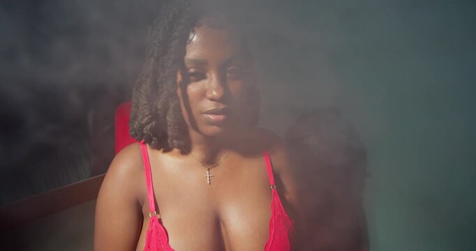 An intimate lifestyle shot of a dark-skinned woman blowing smoke, the orange light dancing on her skin.