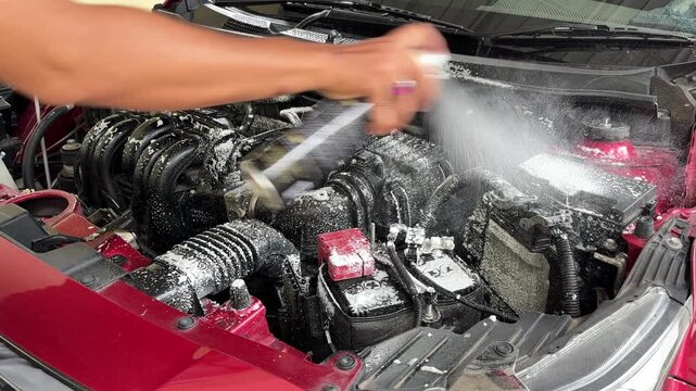 The process of cleaning the car engine compartment by spraying foam liquid into the dirty and dusty engine compartment.