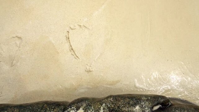 Love sign on the sand with sea wave. Valentine nature concept footage