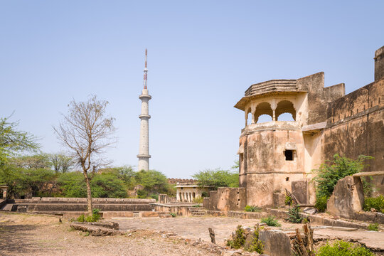 Bundi, India - March 20, 2022: The image shows a tall telecommunications tower rising behind weathered stone walls and an arched pavilion at Taragarh Fort, with dry vegetation and trees under clear