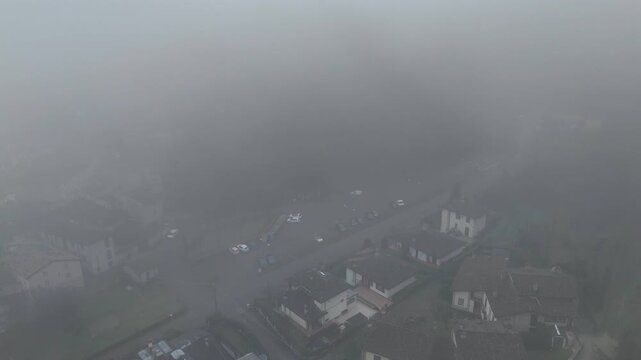 Aerial wide shot of Castell&rsquo;Arquato in Emilia-Romagna, Italy, with medieval houses and streets barely visible through thick winter fog and low visibility atmospheric conditions.