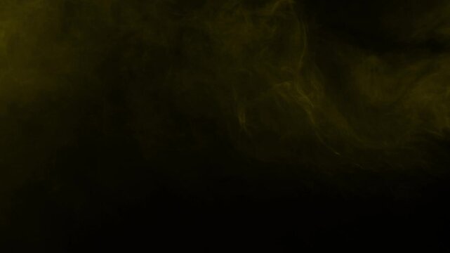Wispy golden yellow smoke and fog gently swirls in place. Isolated on black background, ideal for compositing and visual effects