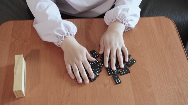 Caucasian woman mixing domino tiles with hands on table. Preparation for educational board game, top view. Mixing dominoes before an intellectual strategy game to develop logic.