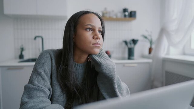 Portrait of pensive black woman thinking about work, sitting at home workplace. Freelancer working out of office, part-time job and online work for people, web designer or developer, female person