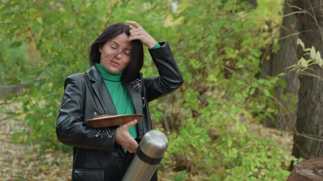 black woman in leather jacket plays tambourine beside thermos in leafy forest, expressive gestures, confident indie rock vibe, green turtleneck, candid portrait, natural light, autumn atmosphere