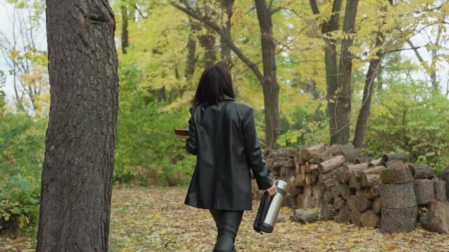 woman in leather jacket carrying guitar, walking past crumbling wall toward stacked logs in goldenleaved forest, autumn leaves carpet ground, moody overcast sky, gritty rock vibe, introspective