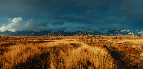 Panorama of field with dry grass, country road, and mountains at sunset, Kyrgyzstan