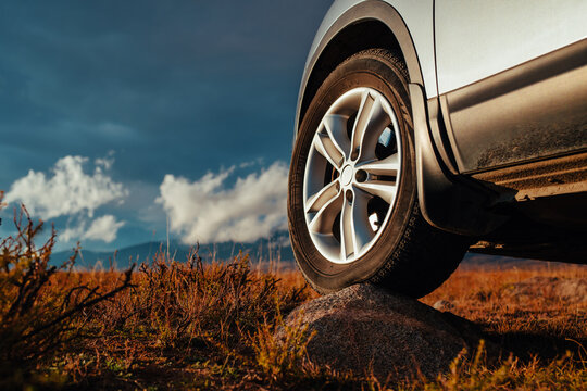 Close-up of car wheel and rim on rock in steppe with mountains and clouds