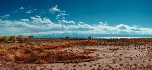 Steppe view panorama of Kyrgyzstan with mountains, lake and clouds on bright sunny day
