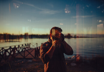 Man taking selfie in window reflection with lake and pier in background