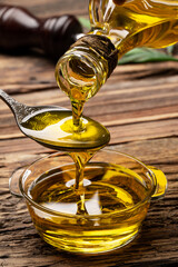 Organic olive oil pouring from carafe  into glass bowl on wooden table
