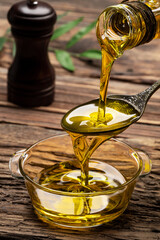 Organic olive oil pouring from carafe  into glass bowl on wooden table