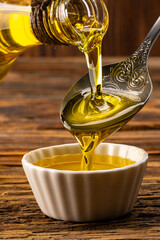 Organic olive oil pouring from carafe  into glass bowl on wooden table